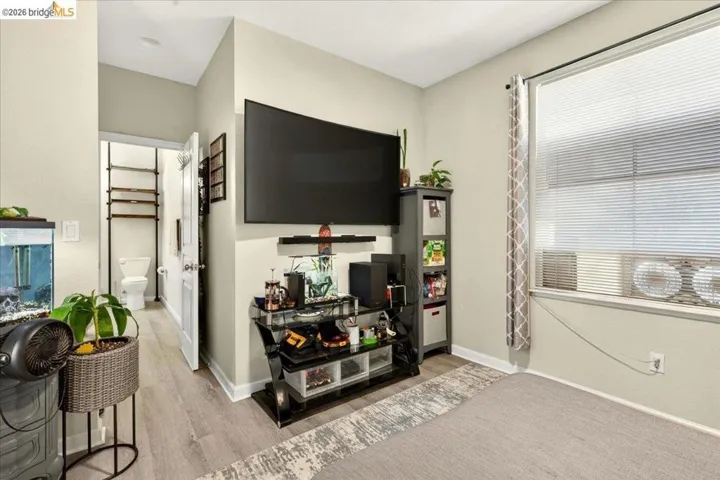 Living area featuring wood-finish flooring, a wall-mounted television, and a large window with blinds