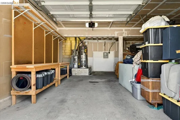 Spacious garage featuring a concrete floor, overhead garage door, built-in wooden shelving, and visible utility access