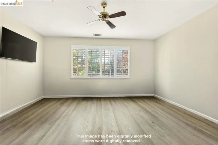Spacious interior room featuring wood-finish flooring, neutral wall tones, and a ceiling fan