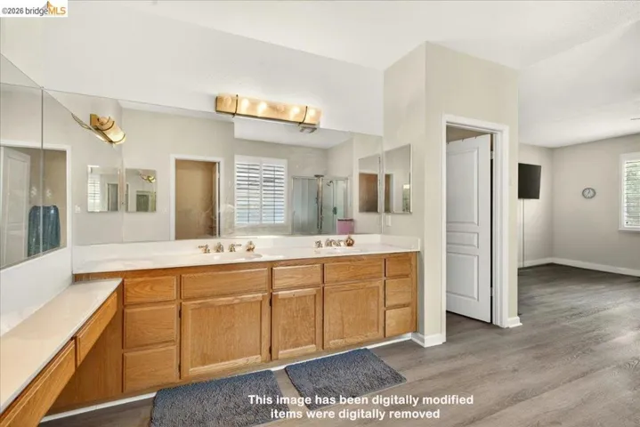 Spacious bathroom with a dual vanity, expansive mirror, wood-finish flooring, and white countertops