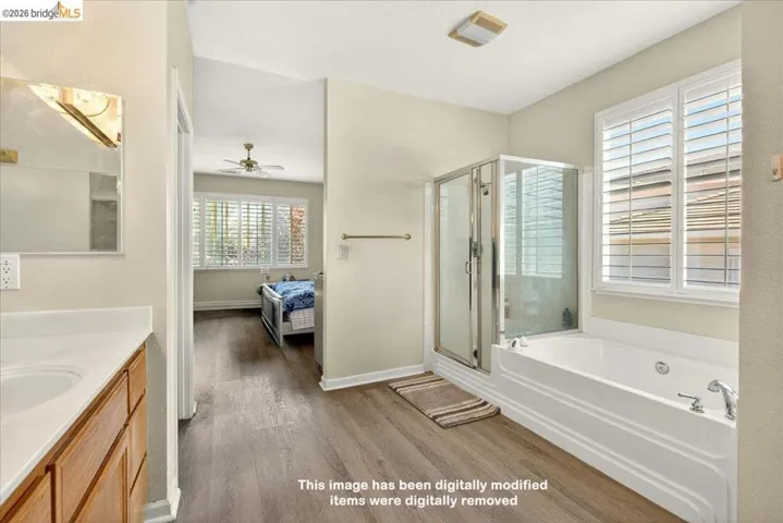 Bathroom featuring a glass-enclosed shower, a built-in jetted tub, wood-finish flooring, a vanity with a white countertop and wood cabinetry, and window shutters