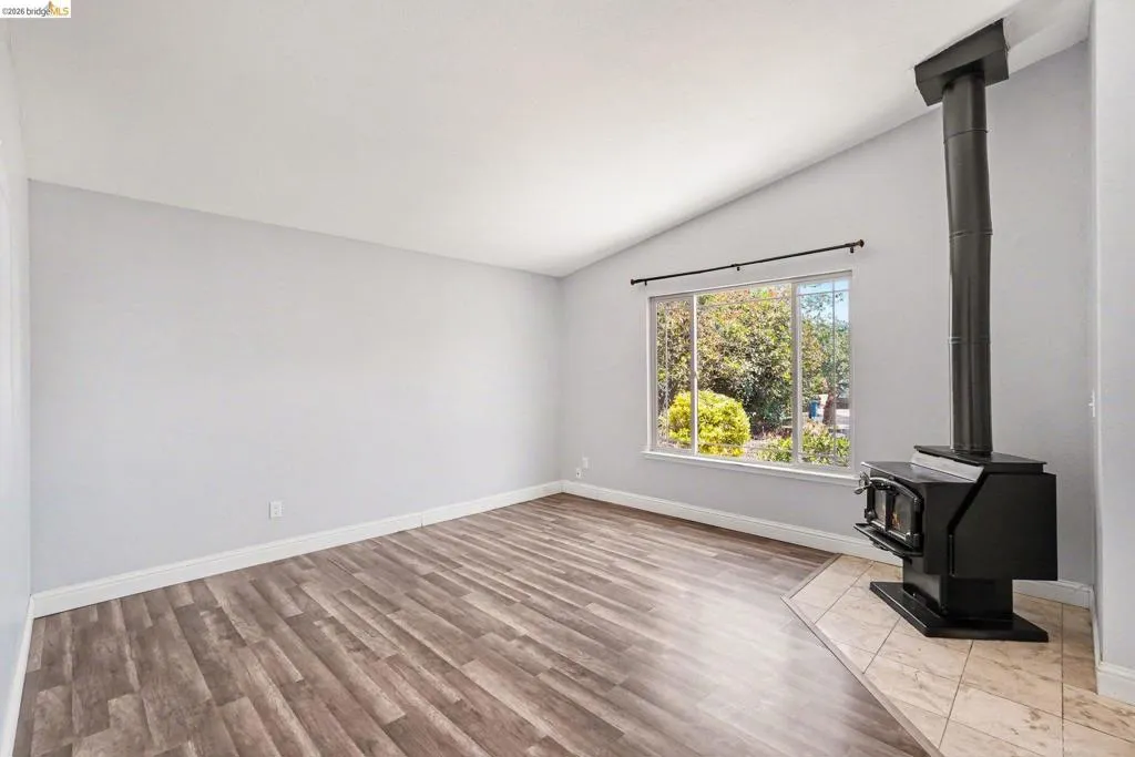 Living area featuring wood-finish flooring, a modern wood-burning stove with a tile hearth, a large window, and vaulted ceilings