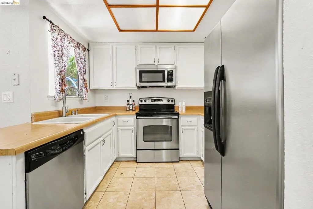 Kitchen featuring white cabinetry, wood-finish countertops, stainless steel appliances, a double basin sink with a gooseneck faucet, and a large ceiling light fixture