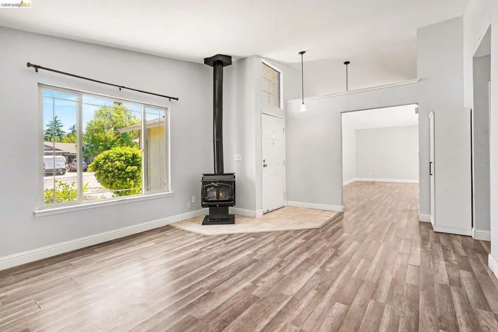 Spacious living area featuring wood-finish flooring, a freestanding black wood-burning stove on a tiled hearth, and large windows