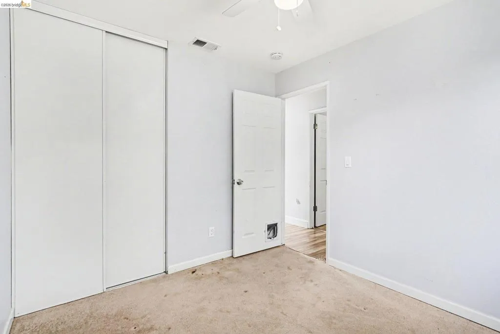 White sliding closet doors, wall-to-wall carpeting, and a ceiling fan