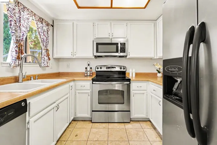 U-shaped kitchen featuring white cabinetry, light wood-finish countertops, and tile flooring