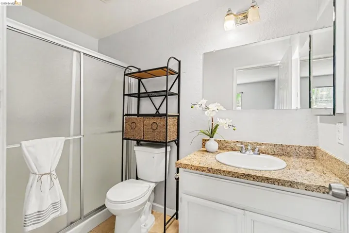 Bathroom featuring a sliding glass shower enclosure, white toilet, and a vanity with a light-colored speckled countertop and white cabinetry