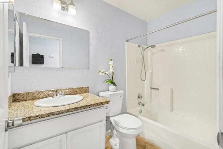 Bathroom featuring a white vanity with a speckled countertop, an oval undermount sink, a white toilet, and a combination shower-tub unit with a white tiled surround