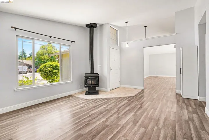 Spacious living area featuring wood-finish flooring, a freestanding black wood-burning stove on a tiled hearth, and large windows
