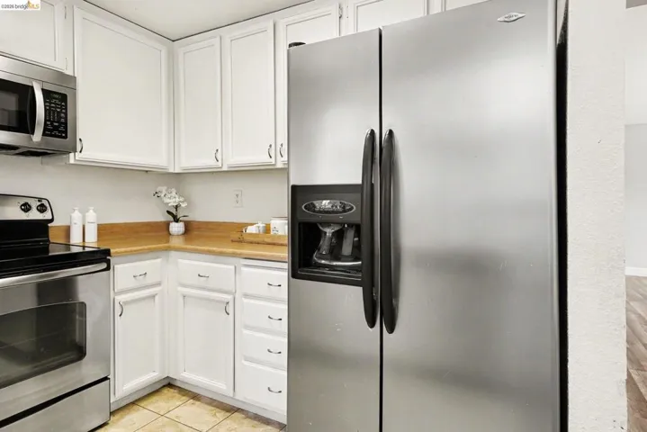 Kitchen featuring white cabinetry with brushed nickel hardware, light wood-finish countertops, stainless steel appliances, and ceramic tile flooring