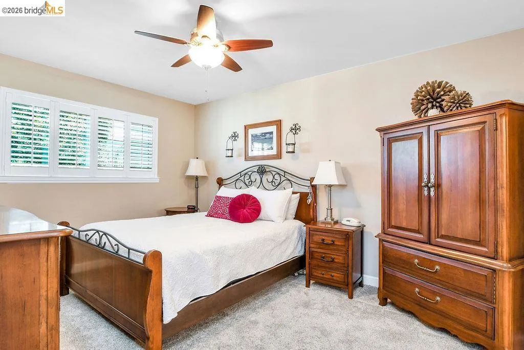 Room featuring light neutral wall paint, white plantation shutters, a ceiling fan with light fixture, and plush carpeting