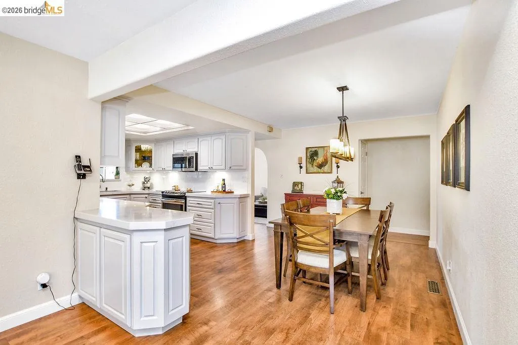 Dining area featuring wood-finish flooring, a contemporary chandelier, and an archway opening to an updated kitchen