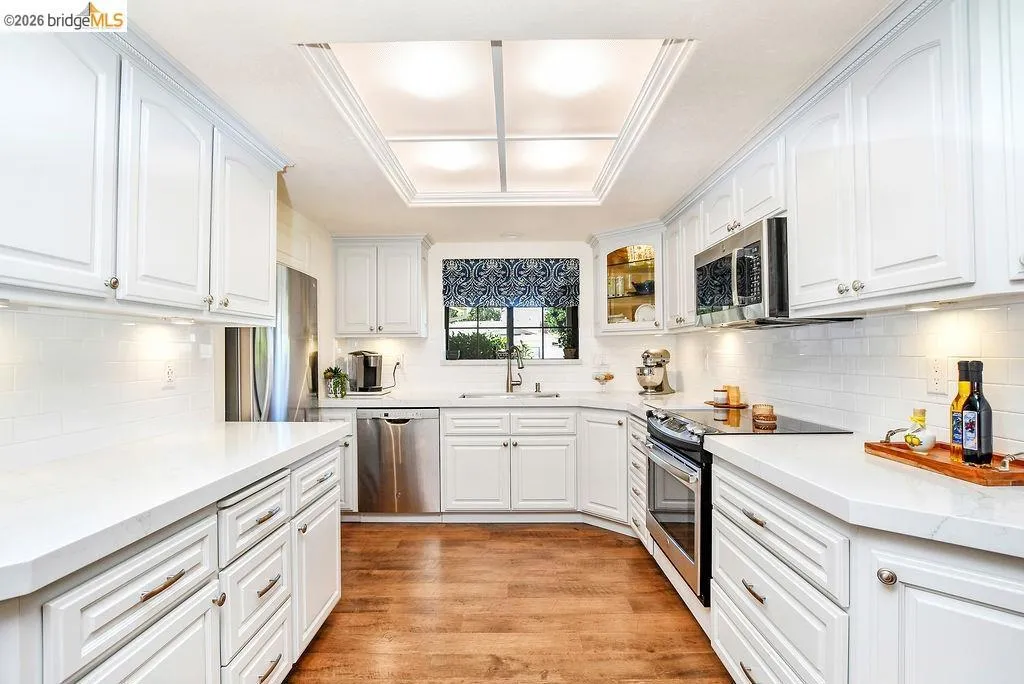 Bright kitchen featuring white cabinetry, light countertops, stainless steel appliances, wood-finish flooring, and recessed ceiling lighting