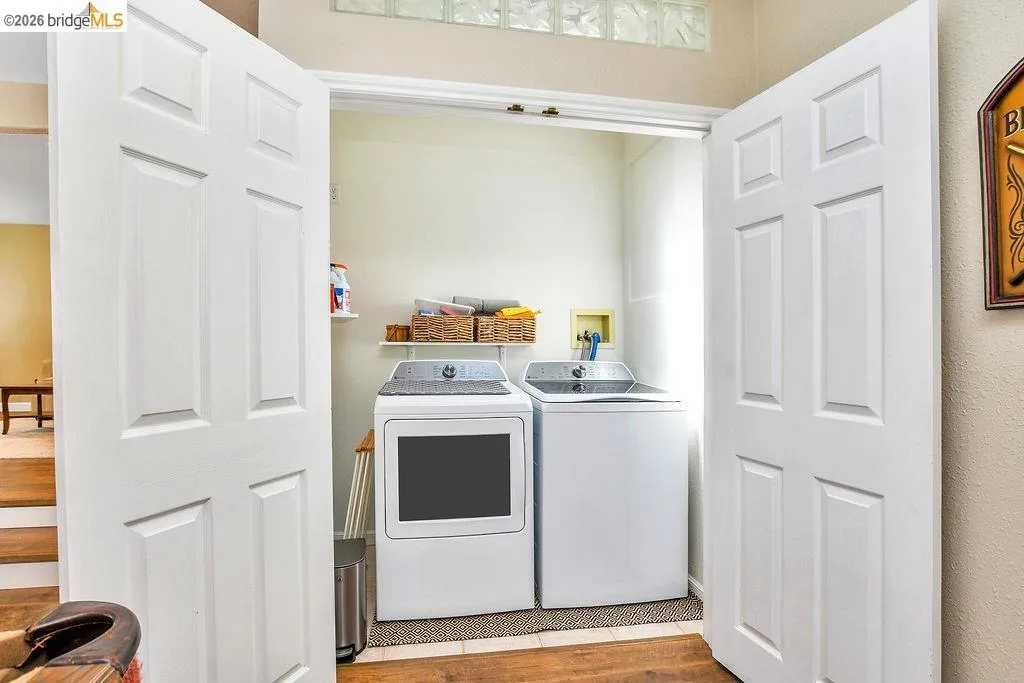 Dedicated laundry area featuring white paneled bi-fold doors, overhead shelving, and glass block window accents