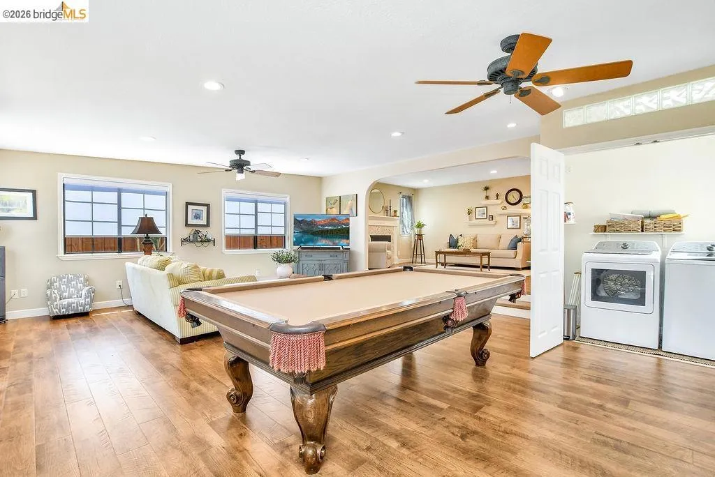 Spacious recreation room featuring wood-finish flooring, two ceiling fans, recessed lighting, and ample natural light from multiple windows