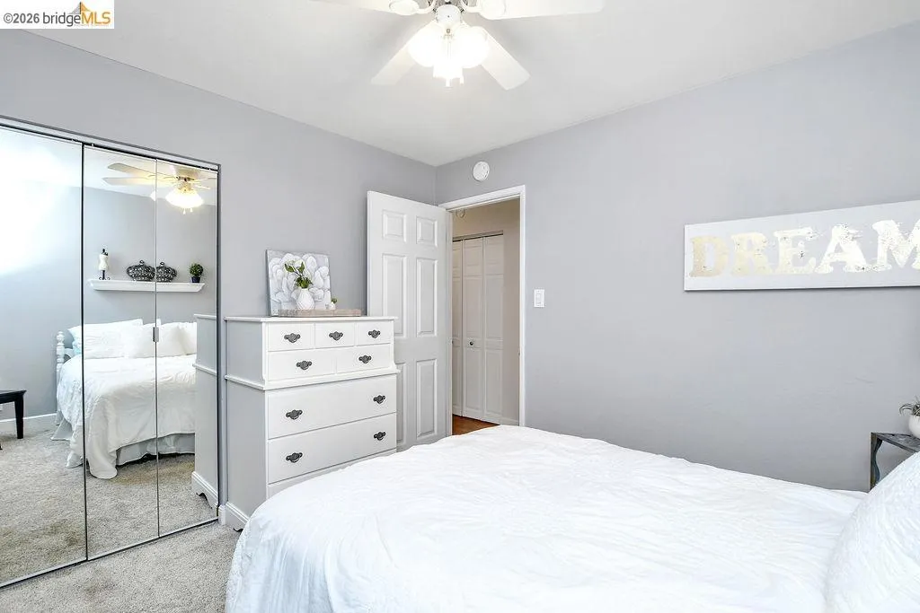 Bedroom featuring light gray wall paint, a ceiling fan with light fixture, carpet flooring, and mirrored closet doors