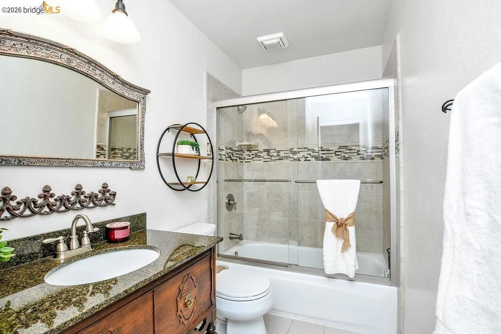 Full bathroom featuring a wood-finish vanity with an undermount sink and dark granite countertop