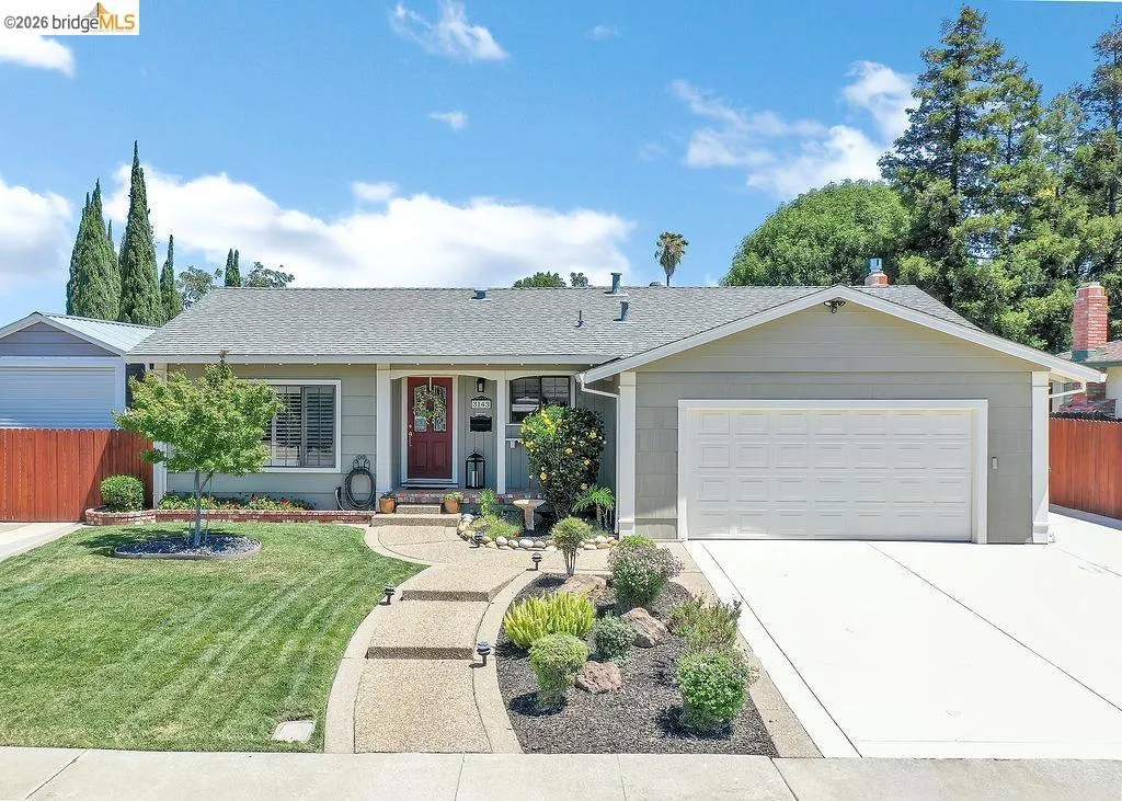 Single-story residence featuring a two-car garage, a concrete driveway, a front lawn, and a curved aggregate pathway leading to the entry