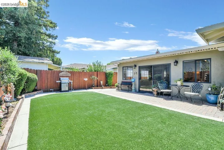 Expansive backyard featuring artificial turf, a paved patio, and a wood privacy fence