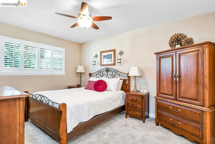 Room featuring light neutral wall paint, white plantation shutters, a ceiling fan with light fixture, and plush carpeting