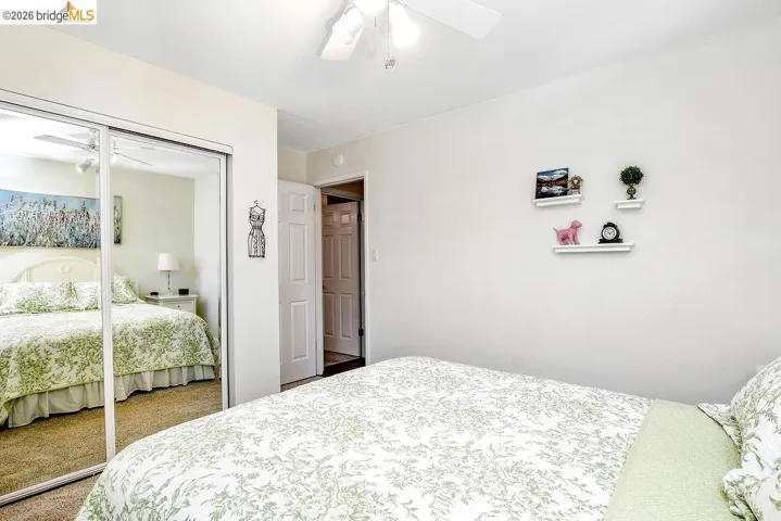 Bedroom featuring mirrored closet doors, a ceiling fan with light fixture, and neutral wall paint