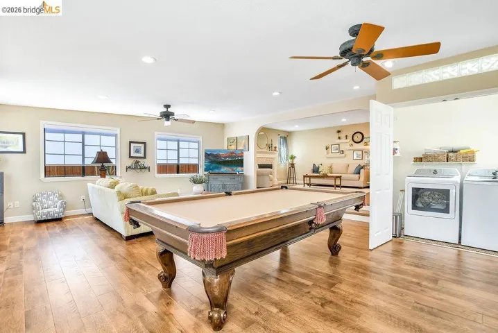 Spacious recreation room featuring wood-finish flooring, two ceiling fans, recessed lighting, and ample natural light from multiple windows
