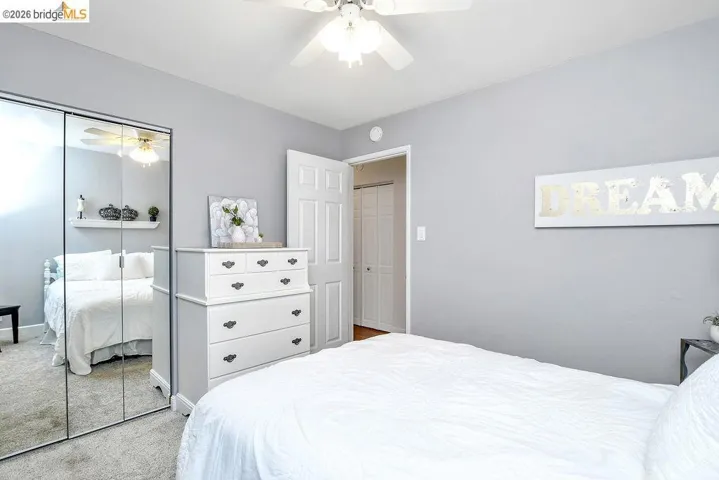 Bedroom featuring light gray wall paint, a ceiling fan with light fixture, carpet flooring, and mirrored closet doors