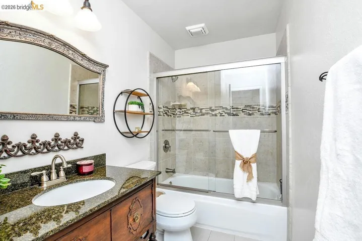 Full bathroom featuring a wood-finish vanity with an undermount sink and dark granite countertop