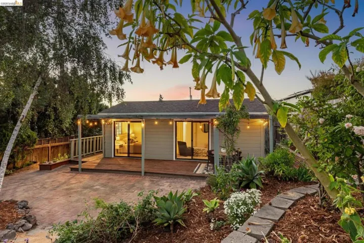 Rear exterior featuring a wood deck, sliding glass doors, string lighting, and a landscaped garden