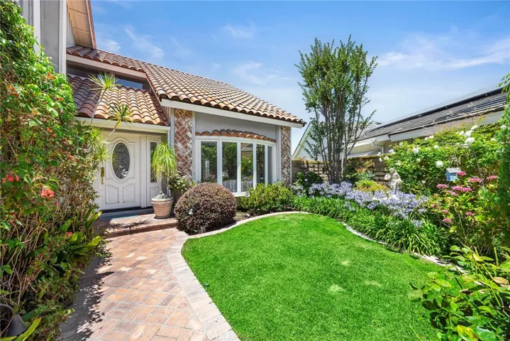 Brick walkway, manicured landscaping, lush green lawn, colorful garden beds, and a welcoming entry that creates a warm first impression.