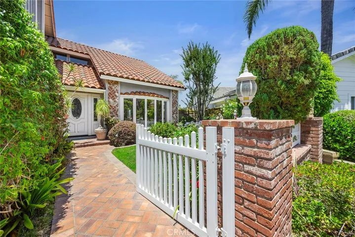 Delightful walkway welcomes you through a private gated entry and beautifully landscaped courtyard. A brick-paved walkway leads to the front door, framed by lush greenery, colorful gardens, and classic brick accents.