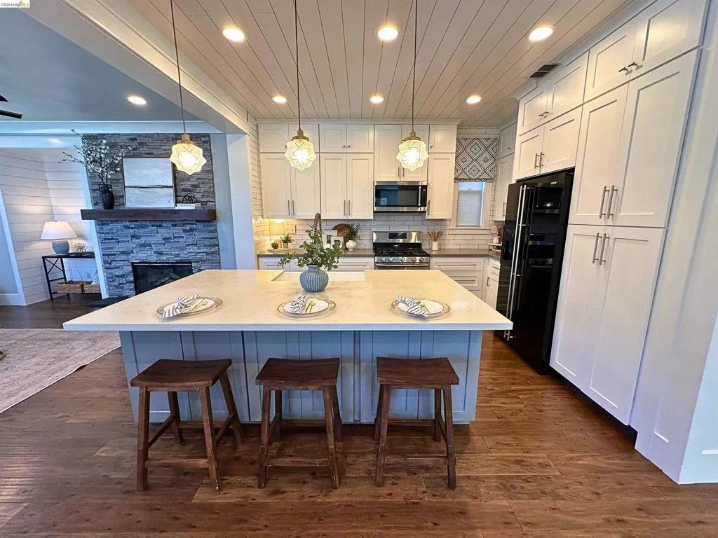 Open-concept kitchen featuring a large island with a light-toned countertop, white cabinetry with silver hardware, wood-finish flooring, and a decorative shiplap ceiling