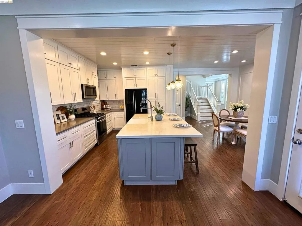 Spacious kitchen featuring white cabinetry, stainless steel appliances, a center island with pendant lighting, stone countertops, and wood-finish flooring