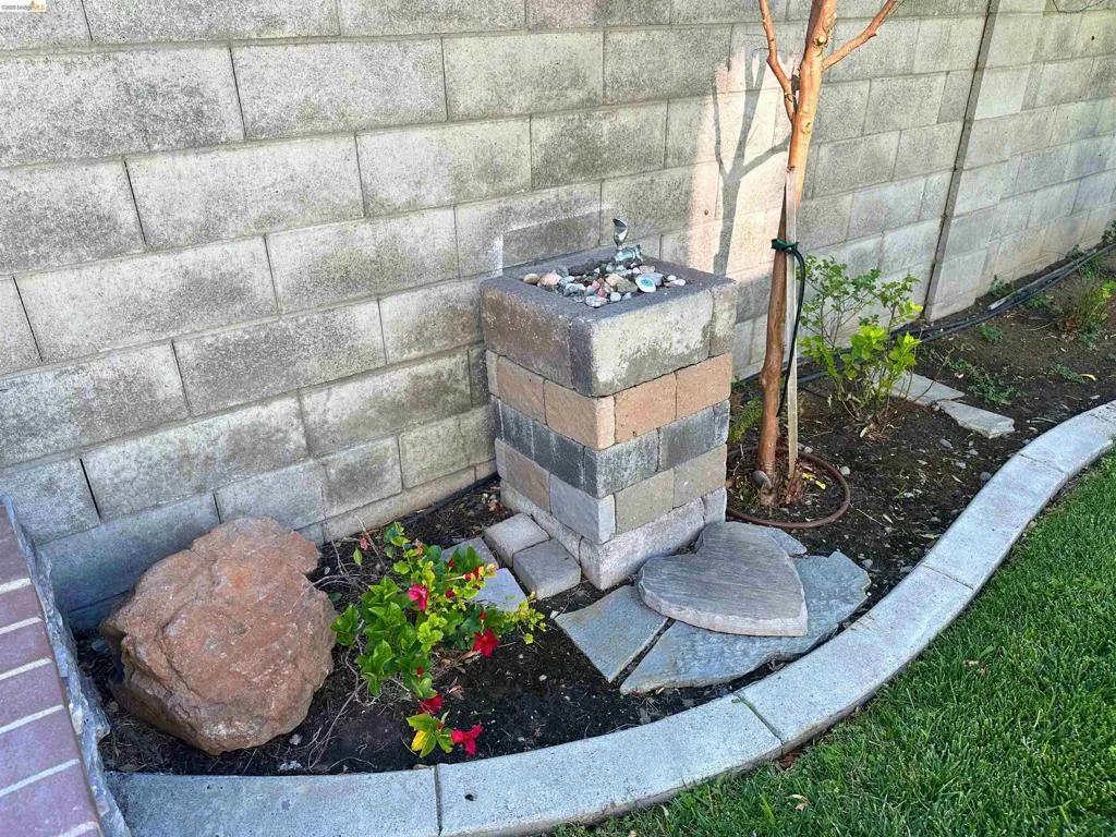 Landscaped garden bed featuring a concrete block retaining wall, a stone water feature, a small tree, and red flowering plants