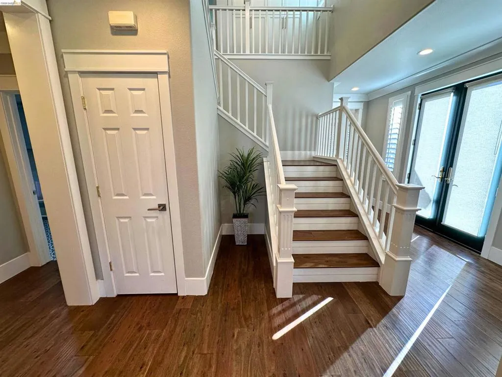 Two-story entryway featuring wood-finish flooring, a white staircase with wood treads, and double glass-paneled doors with transoms