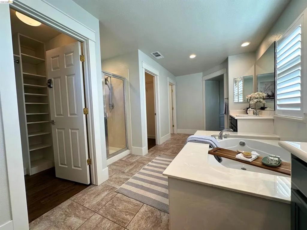 Spacious bathroom featuring a built-in soaking tub with a surrounding countertop, an enclosed glass shower, and a double vanity with mirrored medicine cabinets