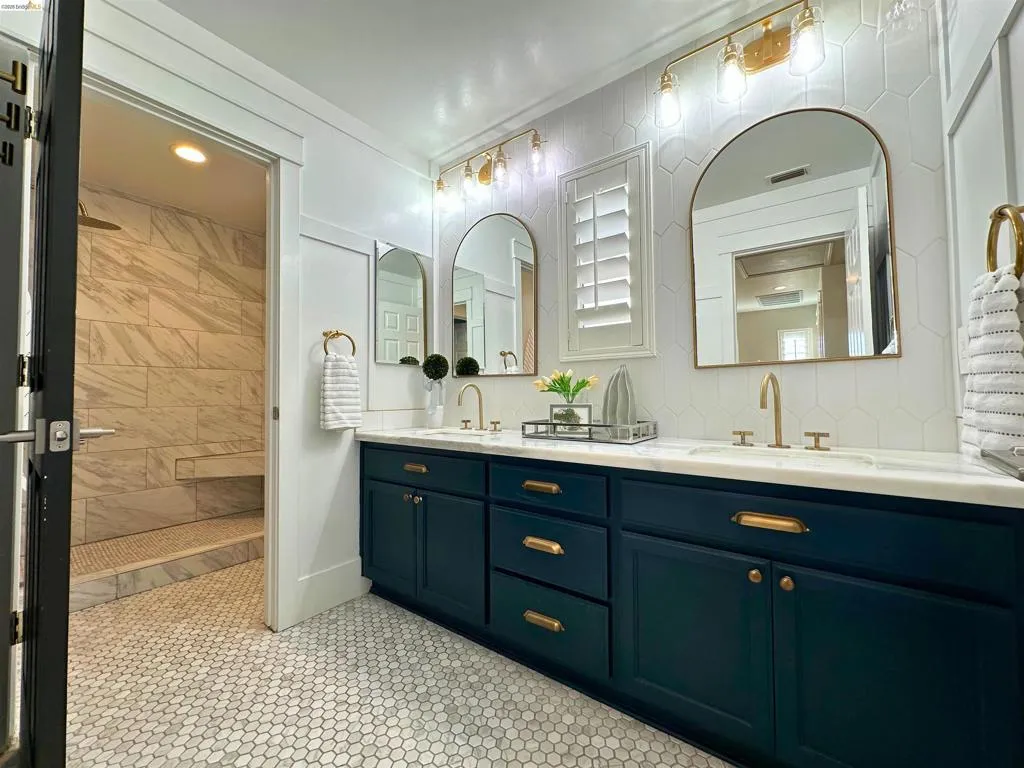 Dual vanity with dark blue cabinetry and brass hardware, featuring a white countertop and two arched mirrors