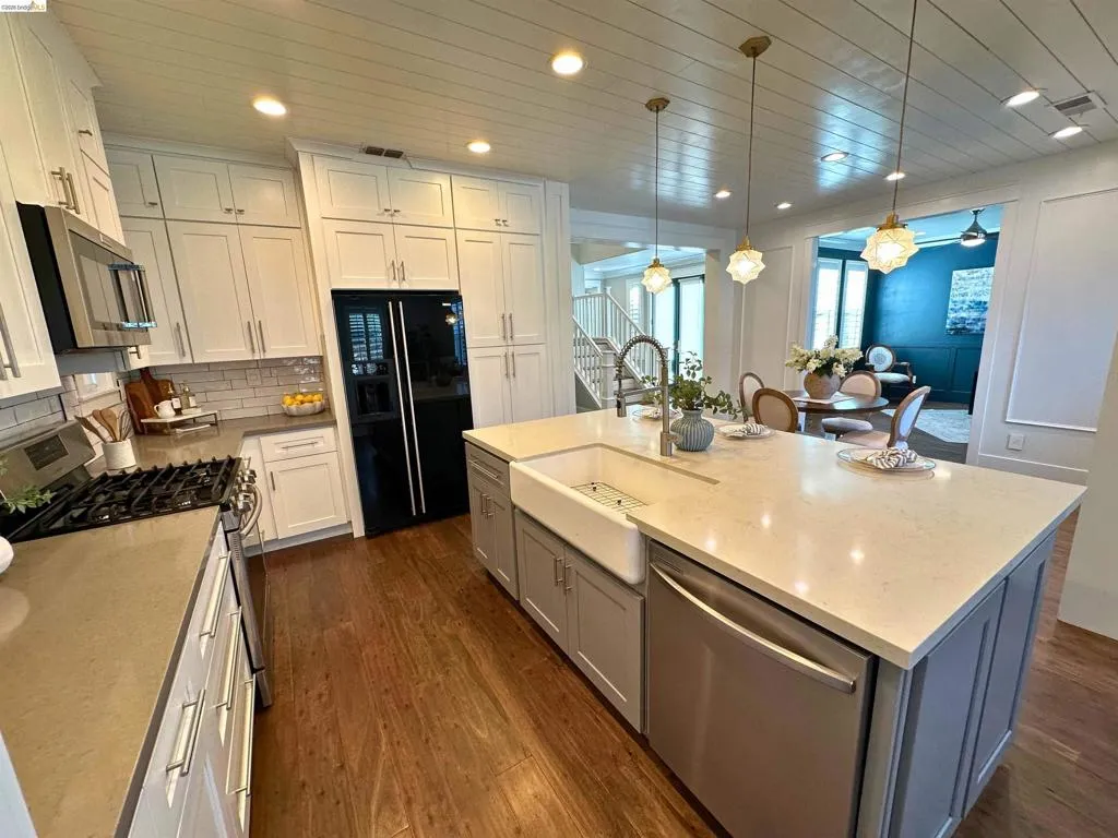 Spacious kitchen featuring a large central island with a farmhouse sink, stainless steel appliances, wood-finish flooring, and extensive cabinetry