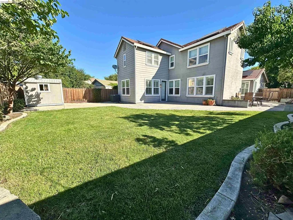 Expansive backyard featuring a manicured lawn, concrete patio, concrete curbing, and a detached storage shed