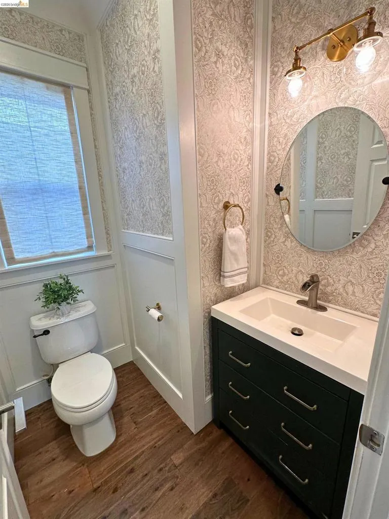 Powder room featuring wood-finish flooring, wainscoting, and patterned wallpaper