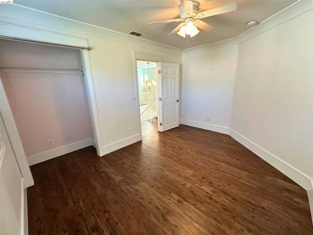Spacious room featuring wood-finish flooring, white baseboards, and crown molding