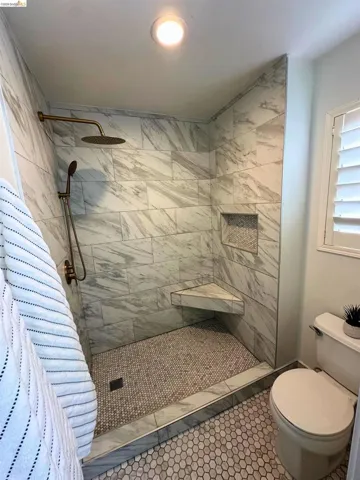 Walk-in shower with large-format tile walls, rain shower head, hand-held sprayer, built-in corner bench, and recessed wall niche
