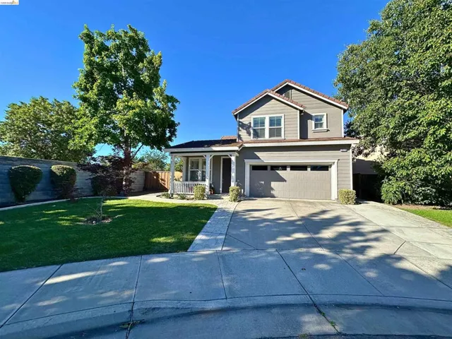 Two-story residence featuring a covered front porch with white railing, an attached garage with a panel door, a paved driveway, a verdant lawn, and mature trees