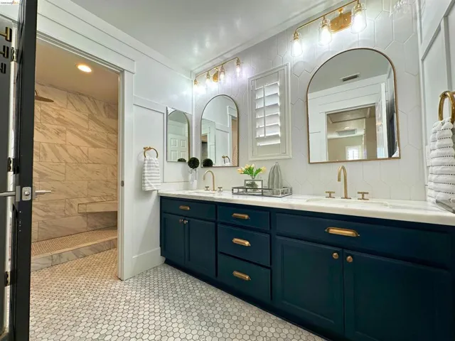 Dual vanity with dark blue cabinetry and brass hardware, featuring a white countertop and two arched mirrors