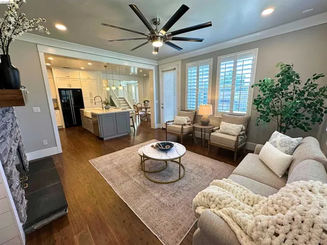 Open-concept living space featuring wood-finish flooring, a stone-clad fireplace, and a contemporary ceiling fan