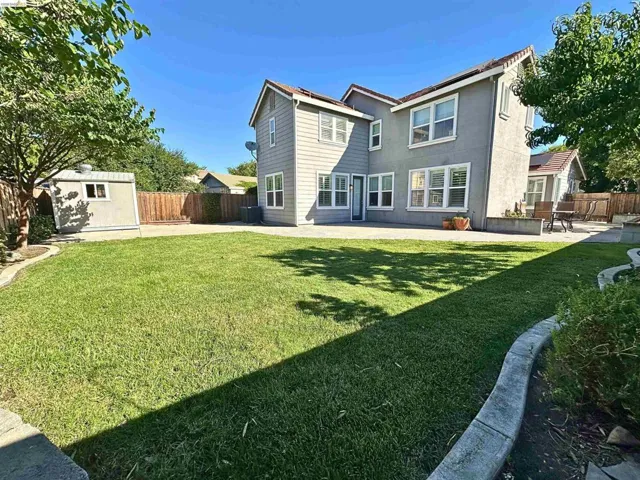 Expansive backyard featuring a manicured lawn, concrete patio, concrete curbing, and a detached storage shed