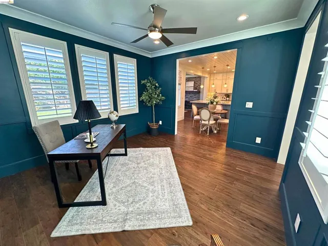 Office space featuring dark teal walls with wainscoting, wood-finish flooring, and white plantation shutters