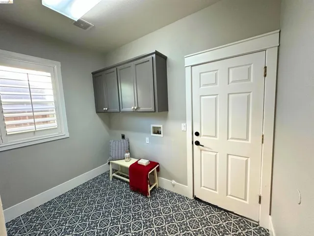 Utility room featuring patterned floor tile, overhead cabinetry, window with plantation shutters, overhead lighting, and a six-panel interior door