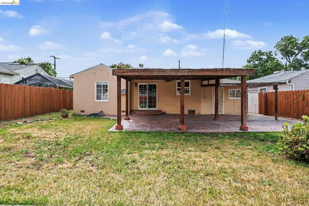Backyard featuring a covered patio with a stamped concrete surface, a stucco exterior, sliding glass doors, and a wood privacy fence