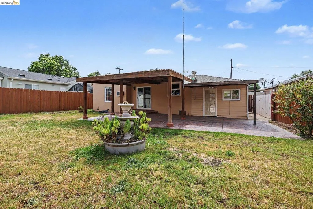 Expansive backyard featuring a concrete patio, wood pergola, and a decorative fountain